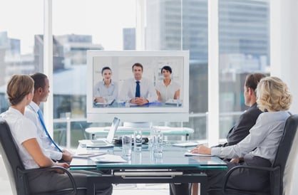Four professionals around a conference table video conferencing with three others