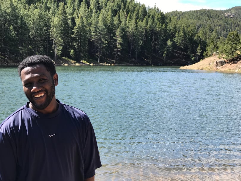 Esubalew standing in front of a scenic lake along a forest of pine trees.